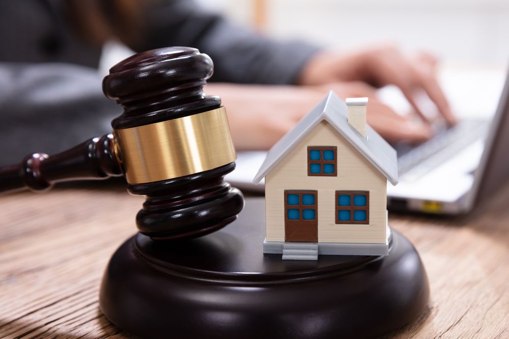 gavel and miniature house with a person typing on a laptop in the background